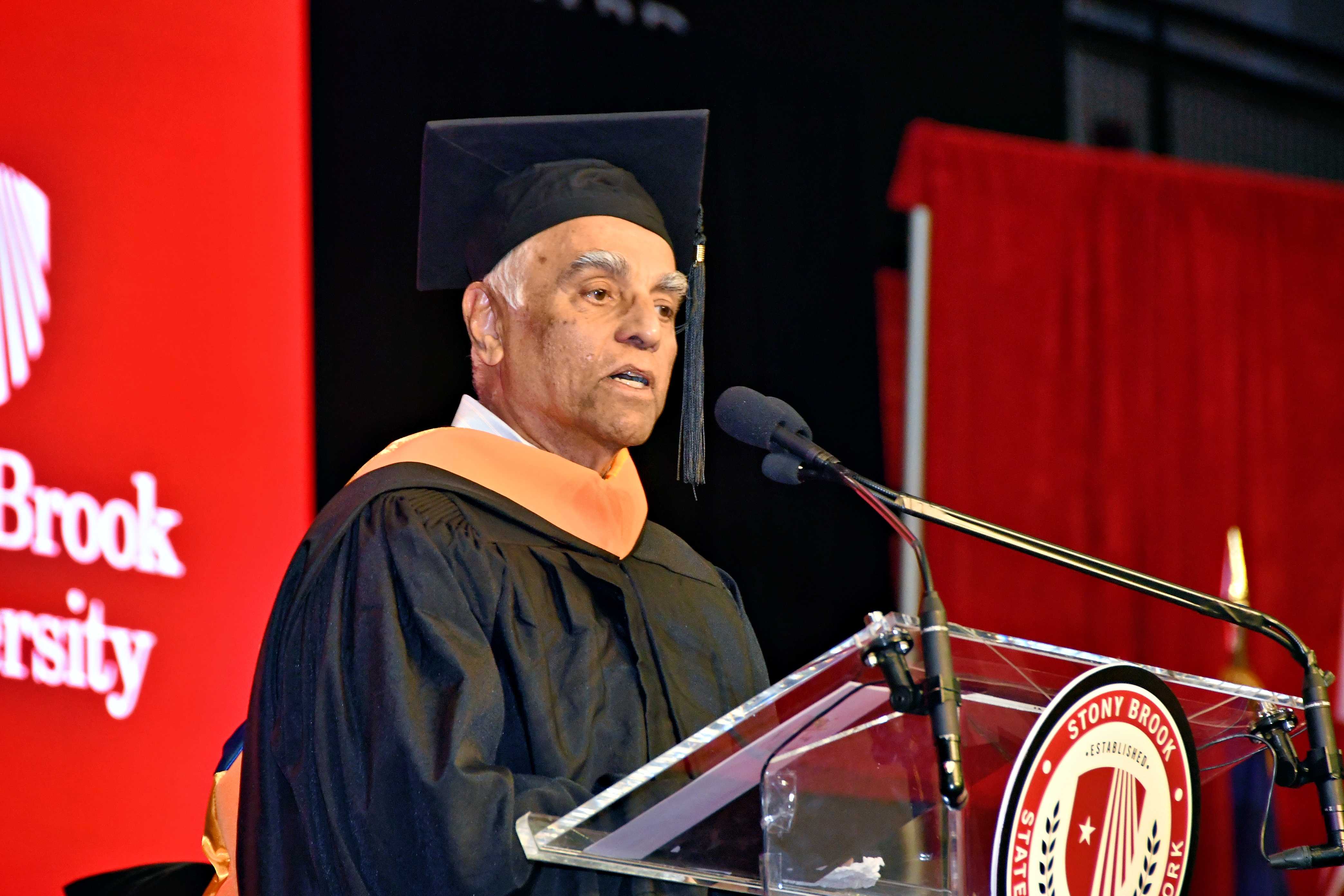 Anant Yardi in academic regalia speaks at a podium during the College of Business Convocation