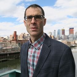 Male wearing glasses stands before a city skyline. 