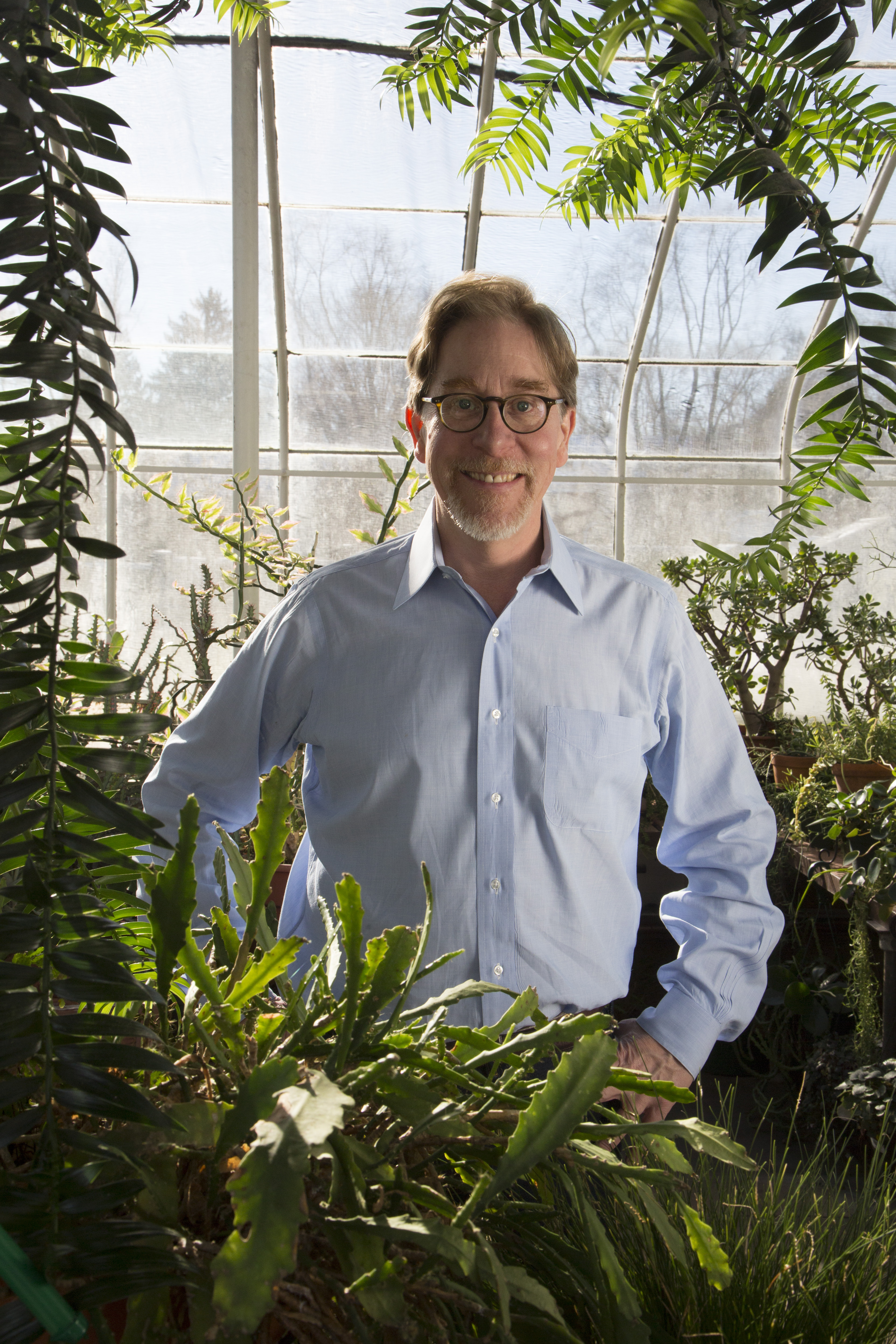 Richard Prum Richard Prums stands behind greenery wearing a blue button shirt