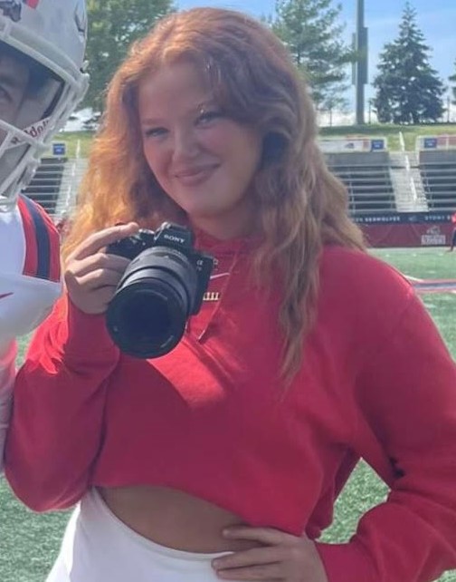 Emelia Bowie holds a camera on the Stony Brook football field.