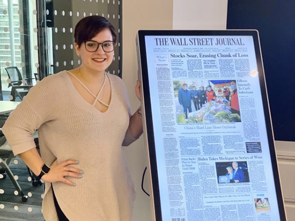 Rachael Eyler stands next to a display of a Wall Street Journal front page